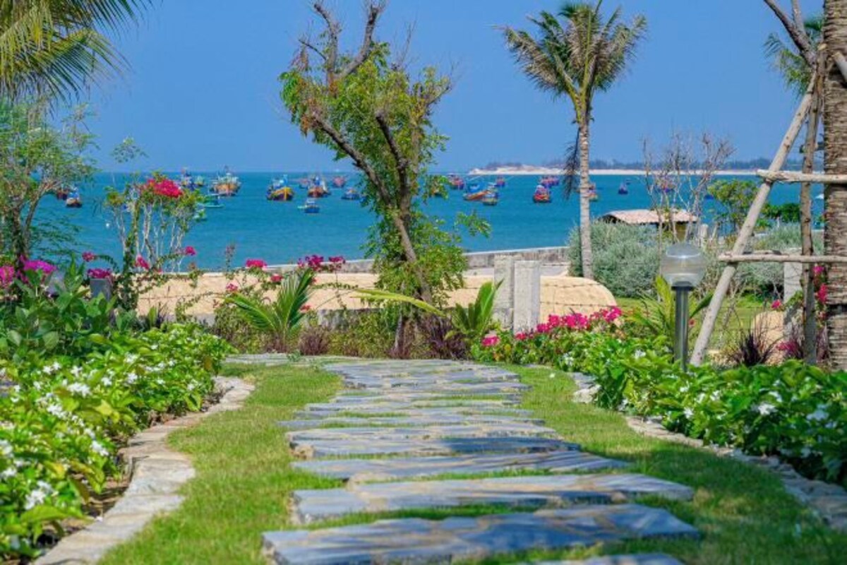 A stone pathway leading to a beach with boats in the water.