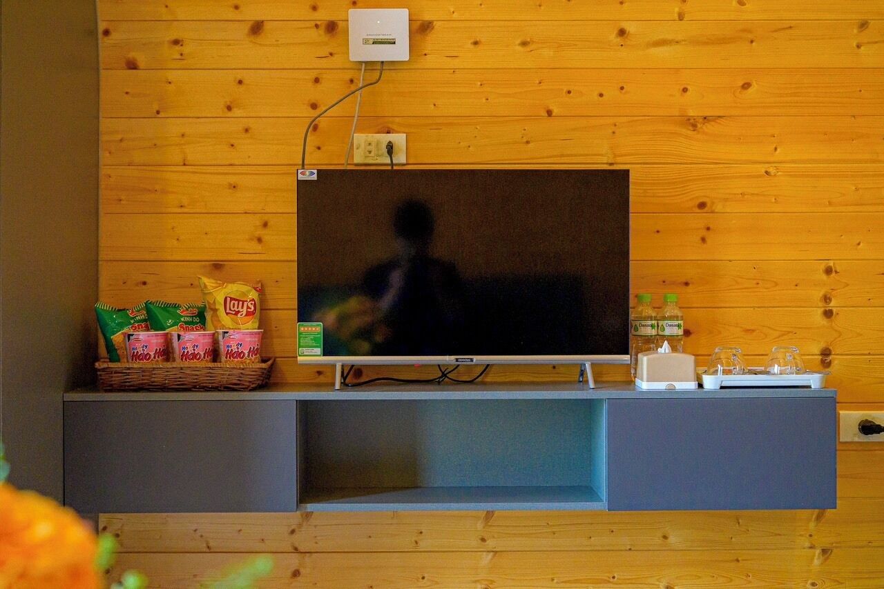 A television mounted on a wooden wall with snacks and a bottle on the shelf below.