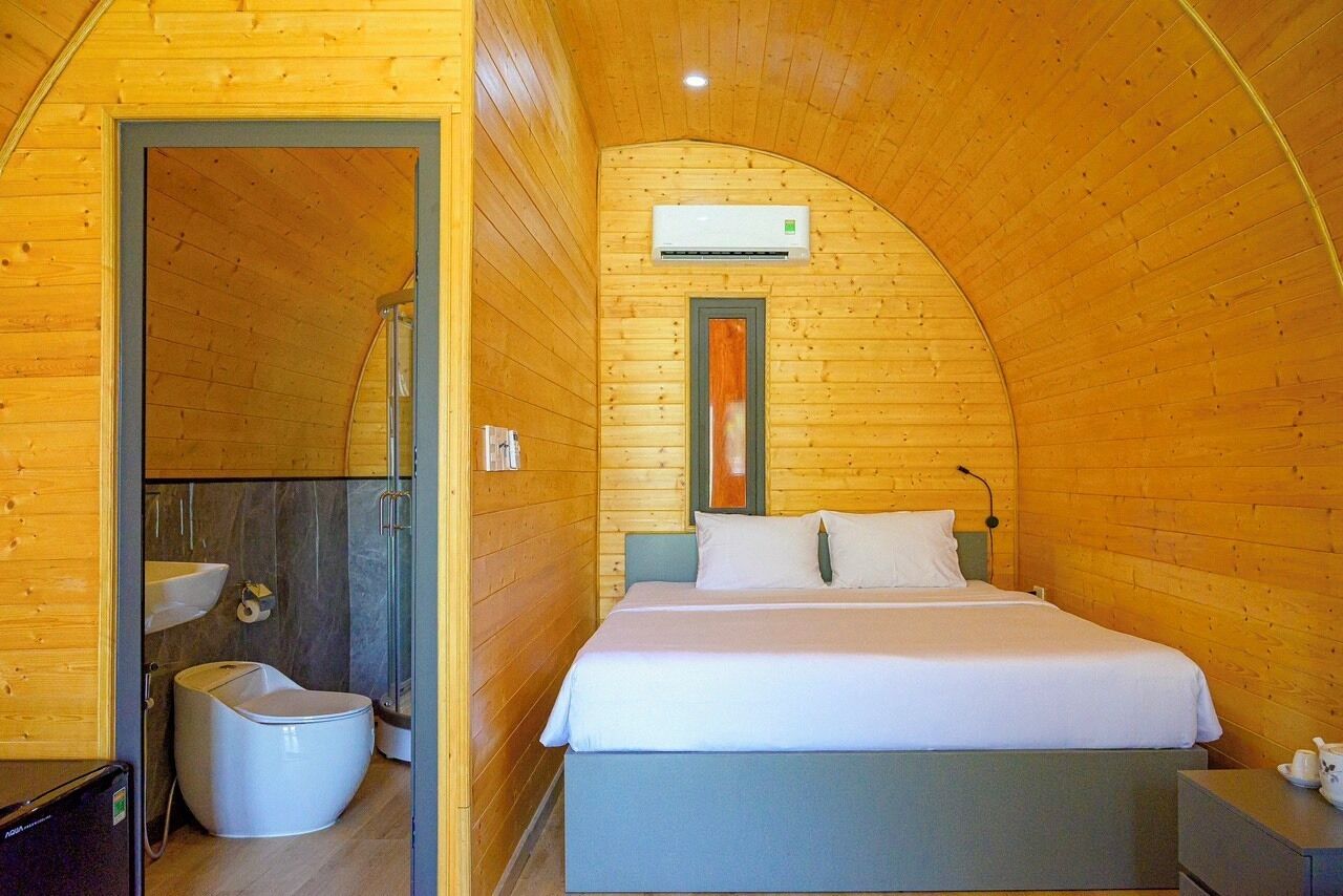 A cozy wooden cabin bedroom with a curved ceiling, a bed, a sink, and a toilet.