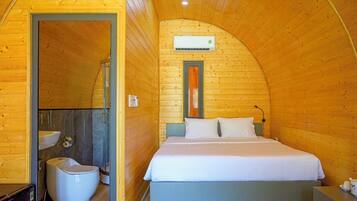 A cozy wooden cabin bedroom with a curved ceiling, a bed, a sink, and a toilet.