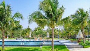 A pool area with palm trees, lounge chairs, and a clear sky.
