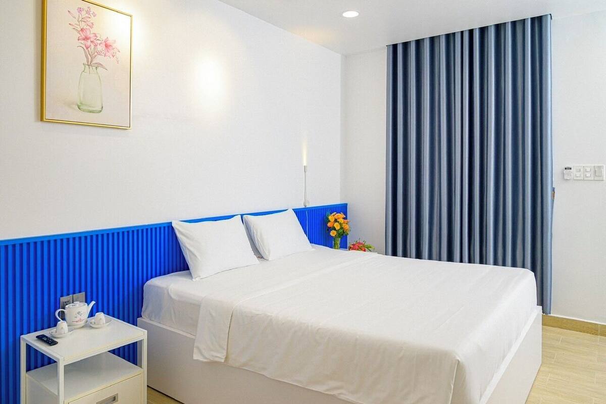 Une chambre d’hôtel avec un lit, une table de chevet avec une télécommande, un vase de fleurs et un tableau au mur.