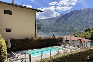 Un espace piscine avec des chaises longues et des parasols, un bâtiment avec un toit rouge et un paysage montagneux en arrière-plan.