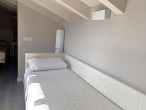 Un lit simple avec une tête de lit blanche, une table de chevet et un luminaire fixé au mur.