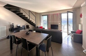 Een moderne woonkamer met een eethoek, een trap en een groot raam met uitzicht op zee.