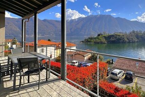 Een balkon met een tafel en stoelen, met uitzicht op een meer en bergen op de achtergrond.