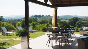 An outdoor patio with a pergola, tables, chairs, and a view of rolling hills. - Agriturismo Podere Ristella - Wine&Food (Roccastrada)