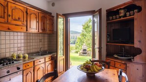A kitchen with wooden cabinets, a tiled backsplash, and a dining table with a fruit bowl. - Agriturismo Podere Ristella - Wine&Food (Roccastrada)