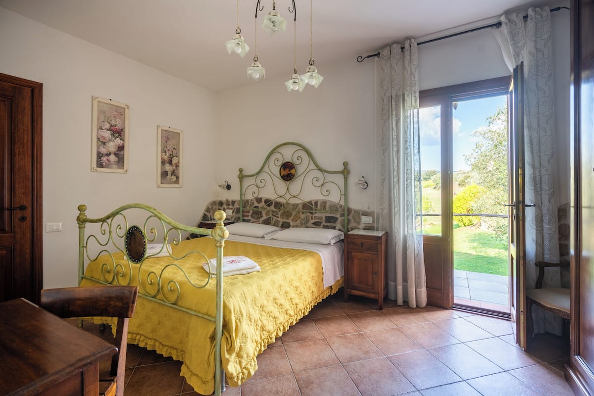 A bedroom with a bed, a wooden chair, a nightstand, and a window with curtains.