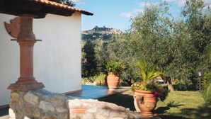 A courtyard with a stone column, potted plants, and a view of a hilltop castle. - Agriturismo Podere Ristella - Wine&Food (Roccastrada)