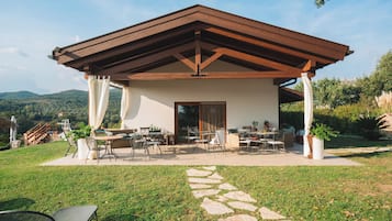 Une terrasse extérieure couverte, avec un chemin de pierre menant à un espace détente agrémenté de tables et de chaises.