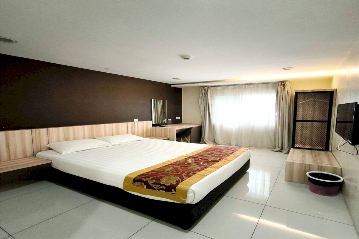 A modern hotel room with a large bed, a desk, a TV, and a bathroom area.