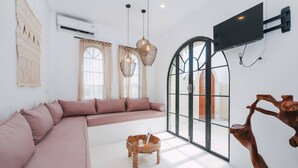 Ein modernes Wohnzimmer mit großem Fenster, einer Couch, einem kleinen Holztisch und einem an der Wand befestigten Fernseher.