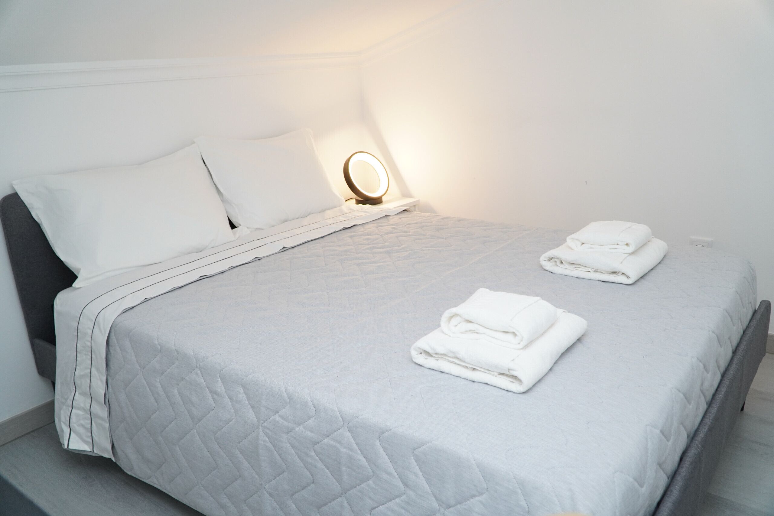 Ein ordentlich bezogenes Bett mit einer gesteppten Tagesdecke, zwei Kissen und zwei gefalteten Handtüchern.