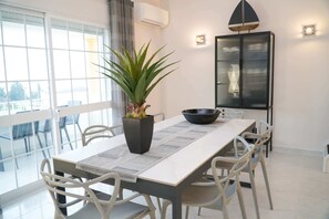 Uma sala de jantar com uma mesa comprida, cadeiras brancas, uma tigela preta, uma planta em vaso e um cardápio.