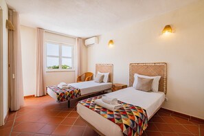 Quarto de hotel com duas camas, uma janela, ar condicionado fixado na parede e luminária na parede.
