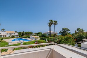 Área residencial com piscina, palmeiras e vista para o mar.