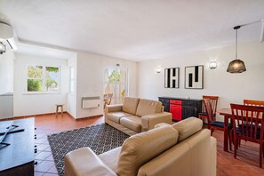 Amplia sala de estar con un juego de sofás, una mesa de comedor con sillas y una cocina visible a través de una puerta abierta.