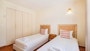 Une chambre d’hôtel avec deux lits simples, une table de chevet en bois, une lampe fixée au mur et une armoire.