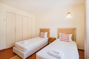 A hotel room with two single beds, a wooden nightstand, a wall-mounted light, and a wardrobe.