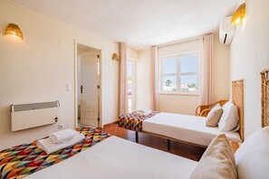 Une chambre d’hôtel avec deux lits, une fenêtre avec des rideaux, un radiateur et une lampe fixée au mur.