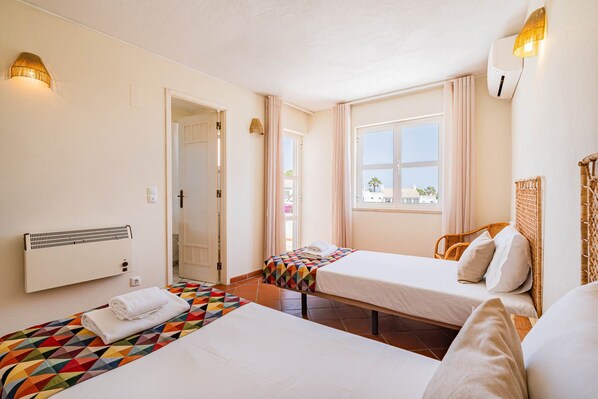 A hotel room with two beds, a window with curtains, a radiator, and a wall-mounted lamp.