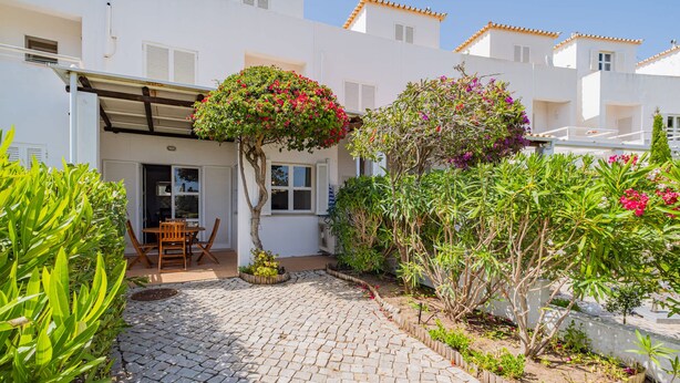 A courtyard with a cobblestone path, a wooden table and chairs, and various plants and shrubs. - Villa Lychee - 350 m from the beach (Guia)