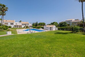 A residential area with a swimming pool, white houses, and well-maintained lawns.