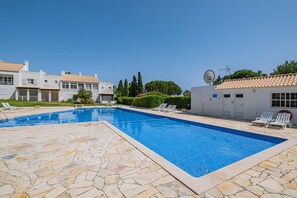 Una piscina con baldosas de piedra, sillones de descanso y un edificio con tejado a juego.