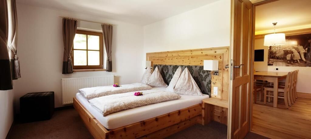 A bedroom with a wooden bed, a small window, and a dining area with a table and chairs.