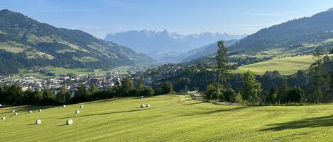 A panoramic view of a valley with a town, green fields, and mountains in the background.