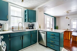A modern kitchen with teal cabinets, a stainless steel dishwasher, and a white countertop.