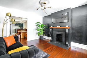 A modern living room with a black sofa, a fireplace, and a dining area in the background.