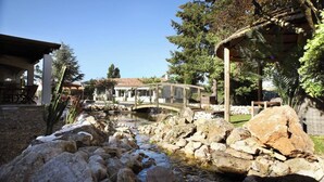 A garden with a small stream, rocks, a wooden bridge, and a building with a tiled roof. - Luxurious Villa with Heated Pool and Jacuzzi in Scenic Nans-les-Pins (Saint-Rémy-de-Provence)