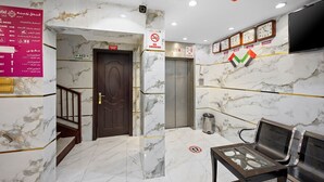 Een hotellobby met marmeren vloeren, een receptiebalie, een bordje 'niet roken', een lift en een zithoek.