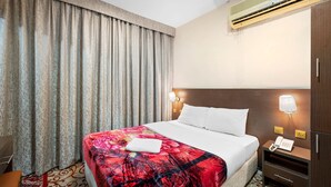 Hotelkamer met een groot bed, nachtkastje met telefoon, wandairco en raam met gordijnen.