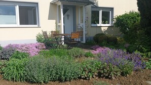 Een huis met een klein terras, een bankje en een tuin vol planten en bloemen.