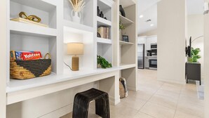 Un salon moderne avec des étagères blanches, une lampe, un panier de livres et un petit tabouret.