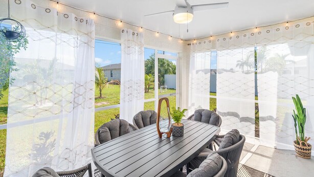 Un patio couvert comprenant une table et des chaises, de grandes fenêtres et un ventilateur de plafond.