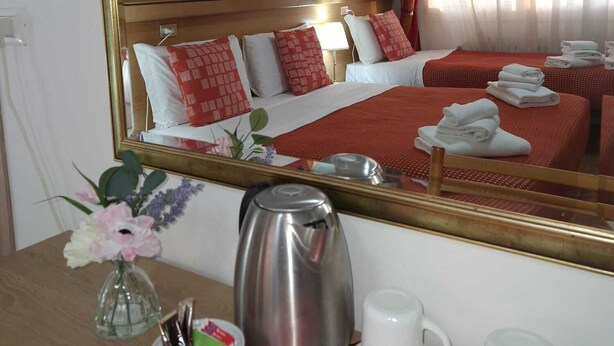 A hotel room with a large mirror, a bed with red bedding, a painting of a cityscape, and a table with a kettle, cups, and a bowl of fruit. - Hotel Tito (Mestre)