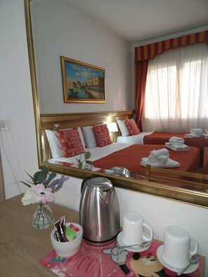 A hotel room with a large mirror, a bed with red bedding, a painting of a cityscape, and a table with a kettle, cups, and a bowl of fruit. - Hotel Tito (Mestre)