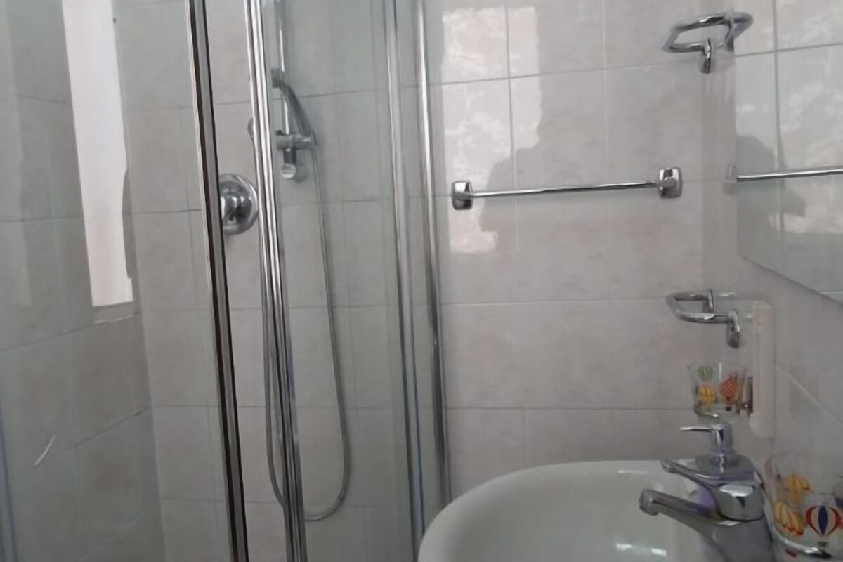 A bathroom with a glass shower enclosure, a white sink, and a towel rack.