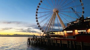A large Ferris wheel at dusk with a wooden pier extending into calm water, overlooking a distant shoreline. - Elektra Muse Studio w/ Views - Walker’s Paradise (Seattle)