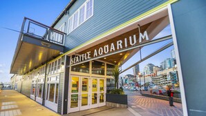 The Seattle Aquarium building with a large glass entrance, a balcony, and a view of the cityscape. - Elektra Muse Studio w/ Views - Walker’s Paradise (Seattle)