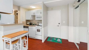 A compact kitchen with white cabinetry, a wooden countertop, a sink, a stove, and a microwave. There is a green mat with kitchen utensils on the floor. - Elektra Muse Studio w/ Views - Walker’s Paradise (Seattle)
