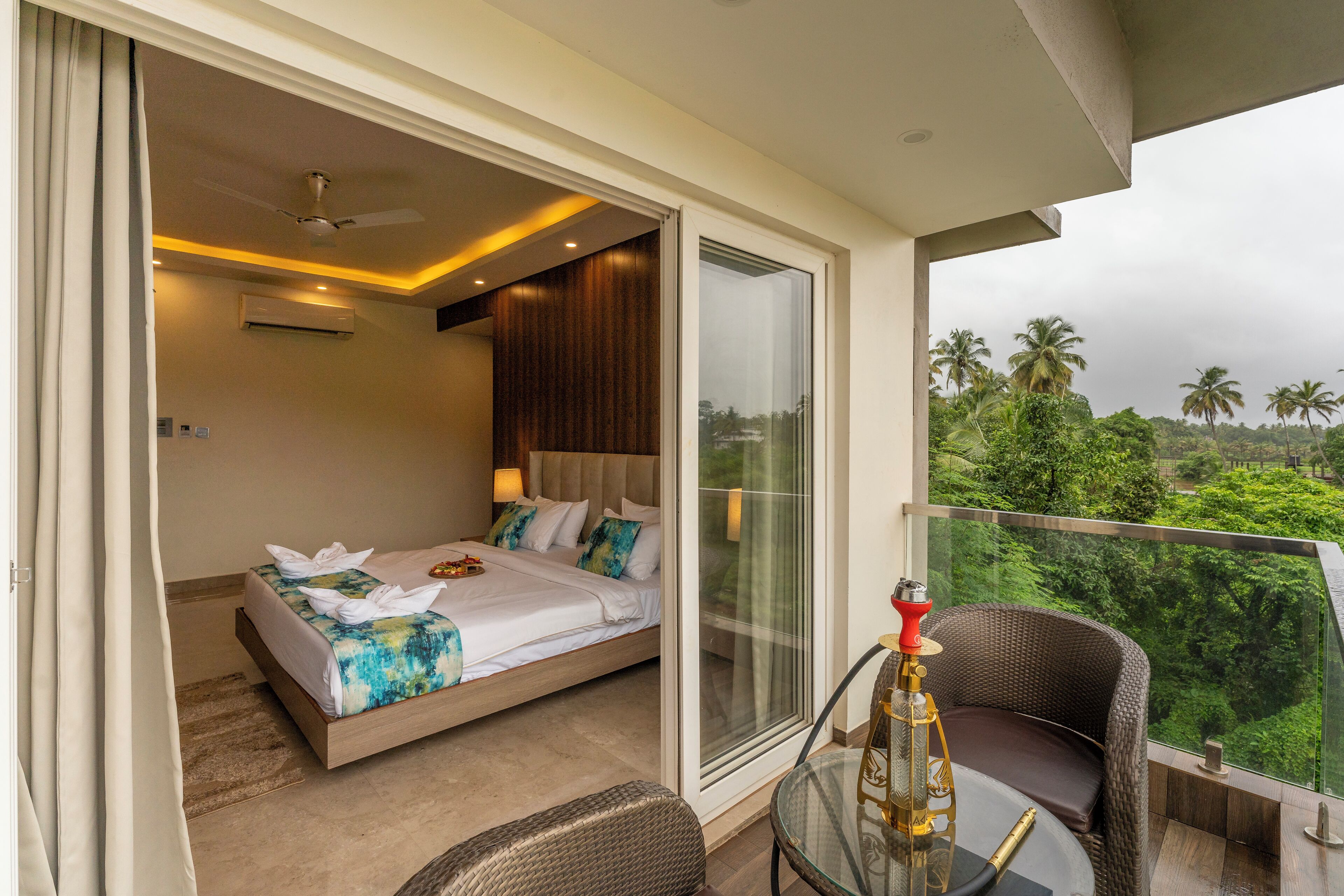 A modern hotel room with a balcony, a bed, a glass table, and a hookah.