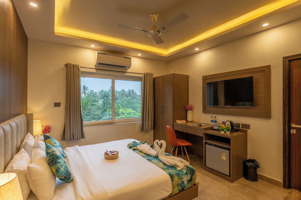 A hotel room with a bed, a desk, a TV, and an air conditioning unit.