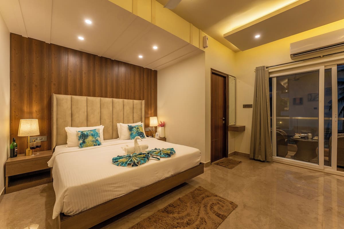 A modern hotel room with a large bed, wooden headboard, and a sliding glass door to the balcony.