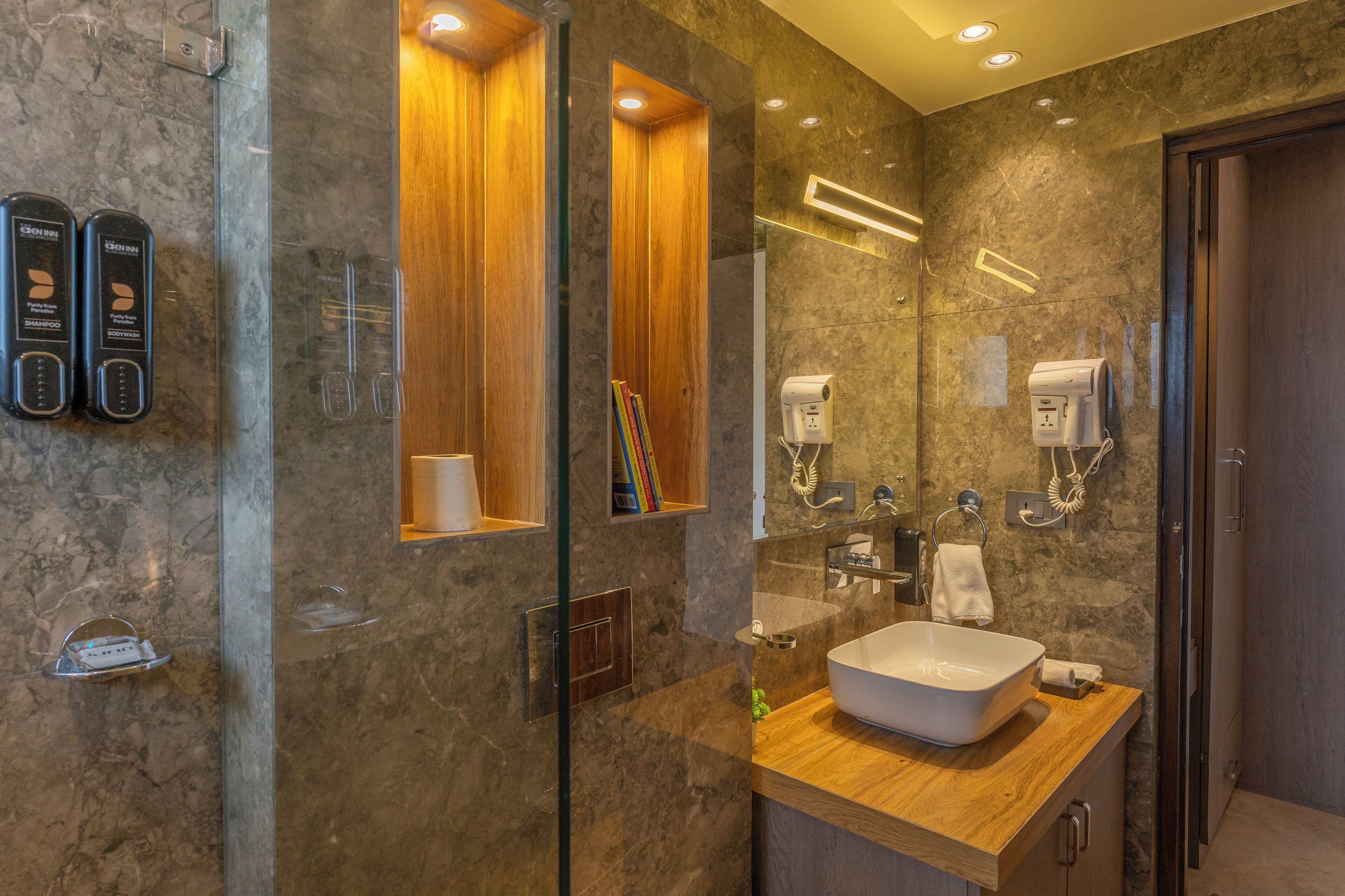 A modern bathroom with a large mirror, wooden vanity, and built-in shelves.