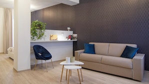 Uma sala de estar moderna com um sofá bege, uma poltrona azul escura e uma pequena mesa branca.